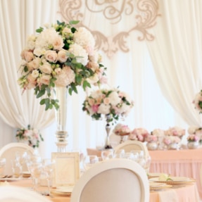 A formal wedding reception breakfast table, with peach and white flowers displayed in a tall, narrow glass vase